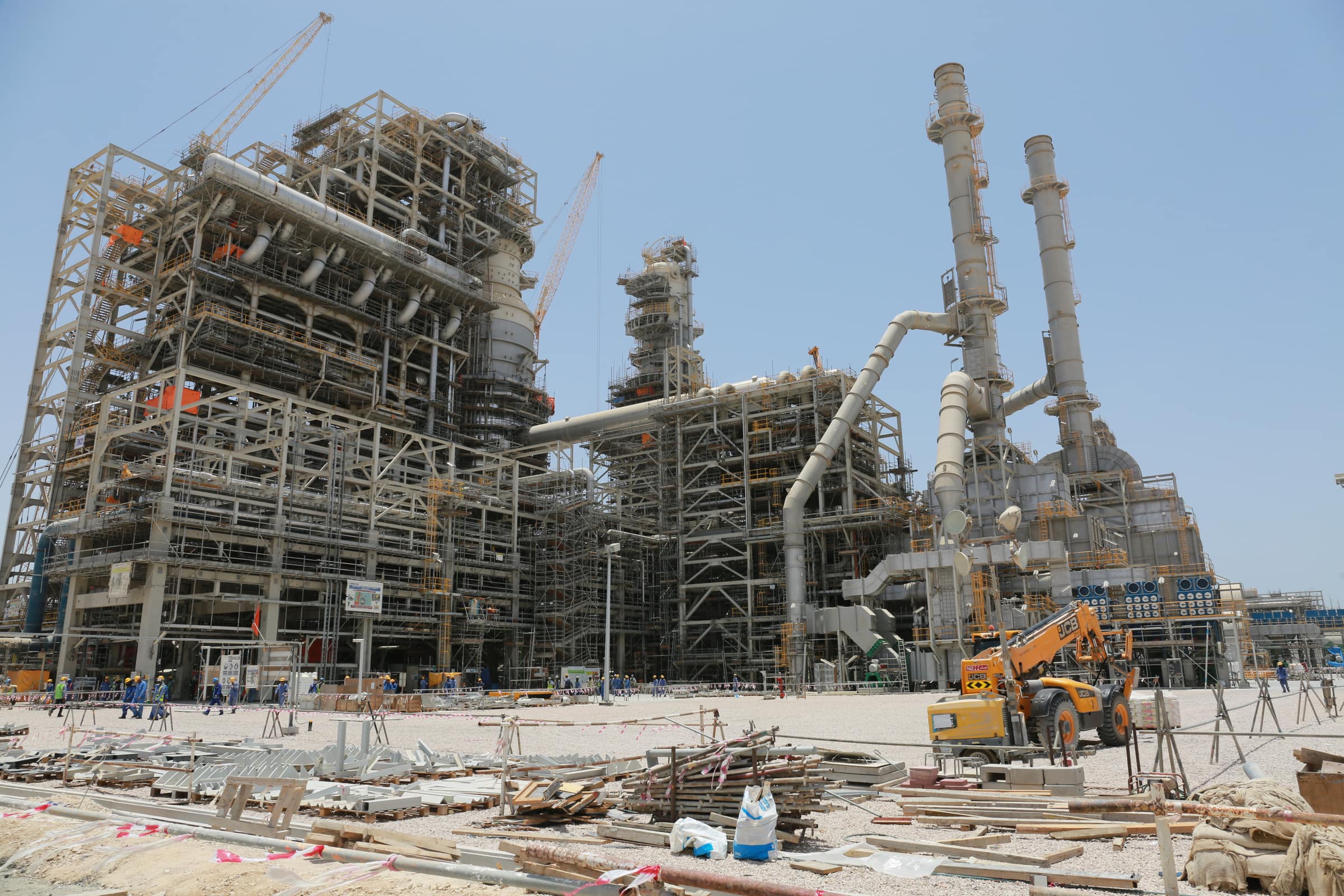 The crude and vacuum distillation units under construction at the Duqm refinery: steel structures, piping and two stacks, with crews on the ground.
