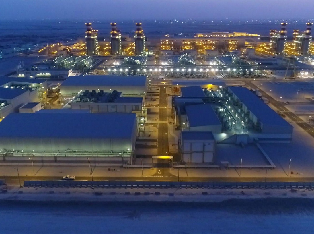 The Umm Al Houl plant at night, seen from the air: lit stacks behind the long plant halls.