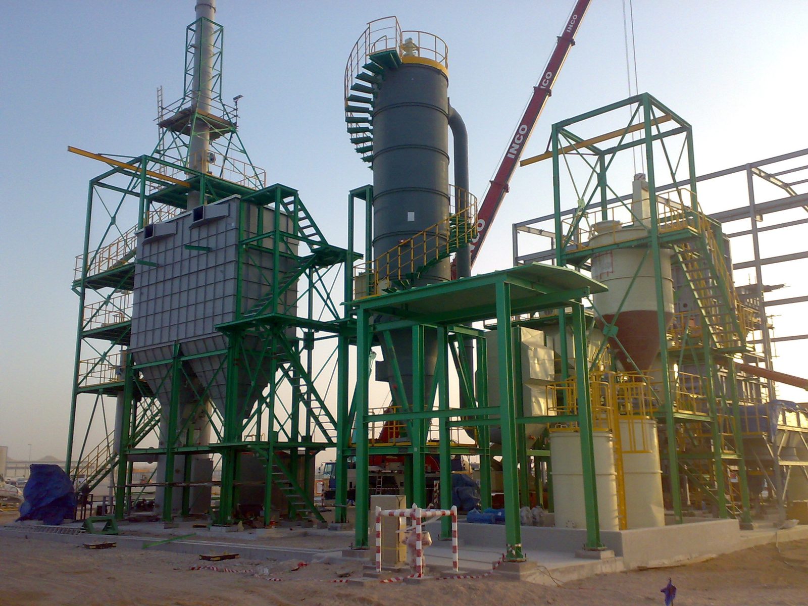 Green steel structures and dust-collection equipment under erection, with a crane behind.