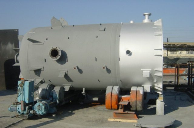 A large horizontal steel vessel with nozzles, on supports in a fabrication yard.