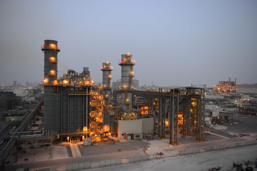 Heat-recovery steam generators and their stacks, lit at dusk.
